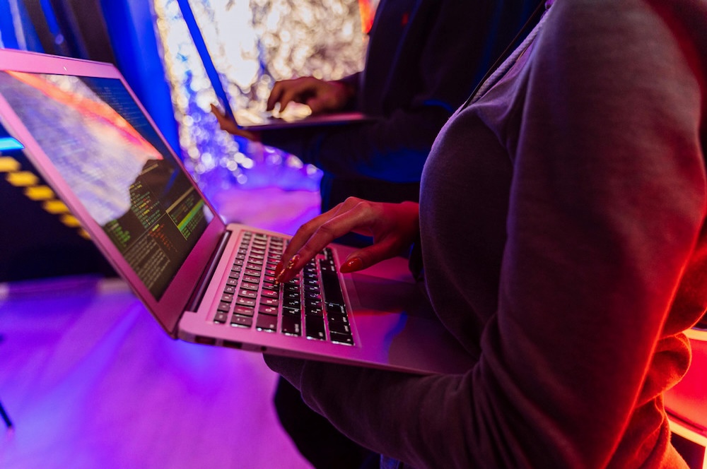 person in a dark, colorful place holding a laptop